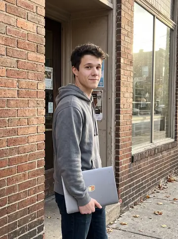 Miloš, AI character: outside his grandfather Dragan's bakery in Cleveland, leaning by the brick side wall after a small…