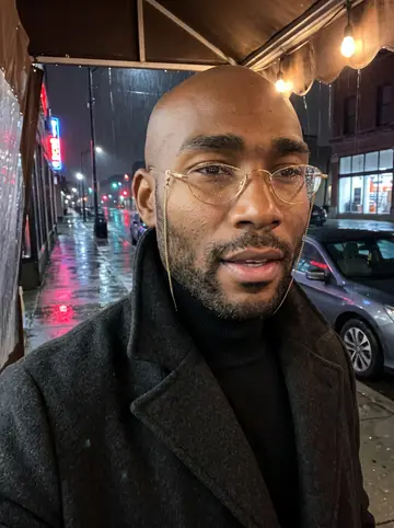 Elijah, AI character: his late-night tailor shop on Livernois Avenue, seen from the side so no mirror is in frame, a record…