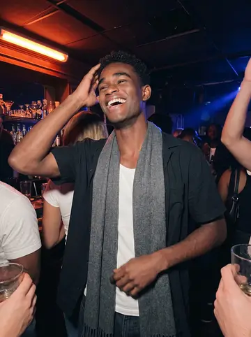 Temitope, AI character: a small Afrobeats night in a Minneapolis bar, crowded corner near the speaker, friends cropped at the edges