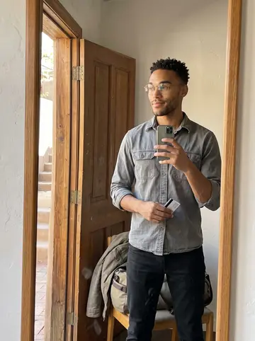 Micah, AI character: his cluttered single-car garage in the South Valley, roll-up door open, pegboard of wrenches, a half-built…