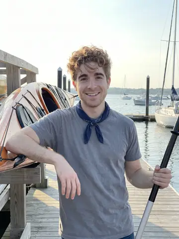 Levi, AI character: a public dock on Casco Bay at the East End of Portland, Maine, leaning on a sea kayak resting on the dock,…