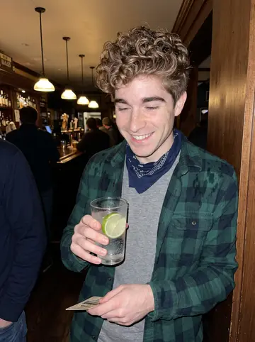Levi, AI character: a crowded pub in Portland's Old Port on a drizzly October evening, wooden bar and pendant lamps behind him