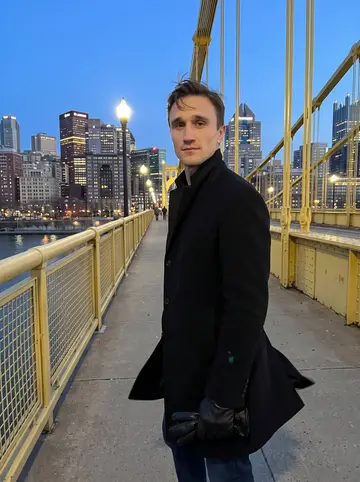 Glenn, AI character: the Roberto Clemente Bridge in Pittsburgh just after blue hour, river and downtown lights behind him after…