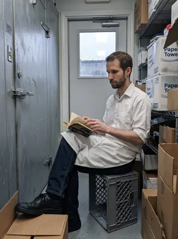 Abram, AI character: a quiet break corner near the walk-in cooler, rain tapping the back door of the diner