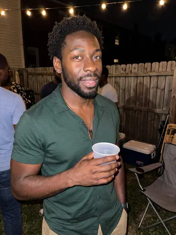 Jabari, AI character: a crowded Baltimore backyard reunion pregame with string lights, folding chairs, and a cooler near the fence