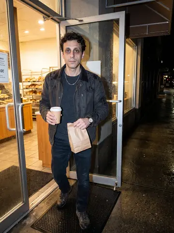 Anthony, AI character: under the awning of the bakery below his apartment at 4 a