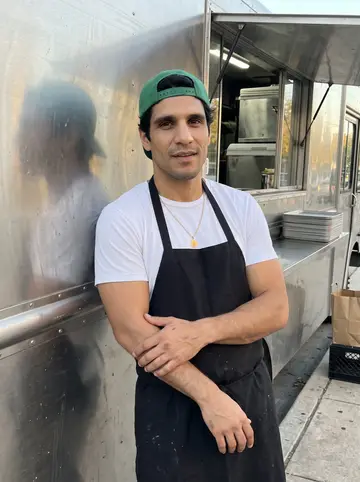 Emilio, AI character: the sidewalk beside his parked birria taco truck on East Cesar Chavez in Austin, leaning on the side of…