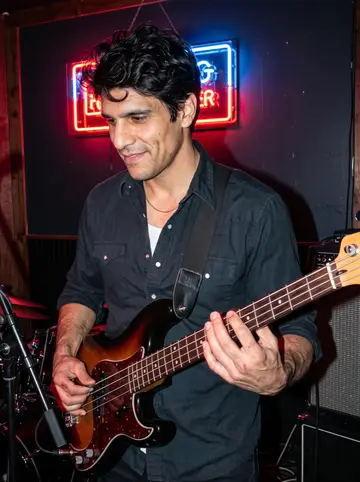 Emilio, AI character: the small stage of an East Austin bar on a Tuesday night, a bandmate's amp and a neon beer sign behind him