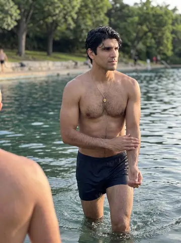 Emilio, AI character: Barton Springs pool in Austin at dawn, the limestone edge and trees behind him